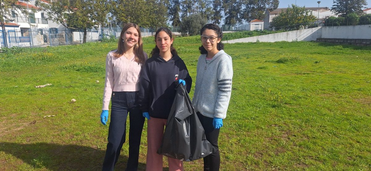 Três alunas com sacos de lixo no campo verde